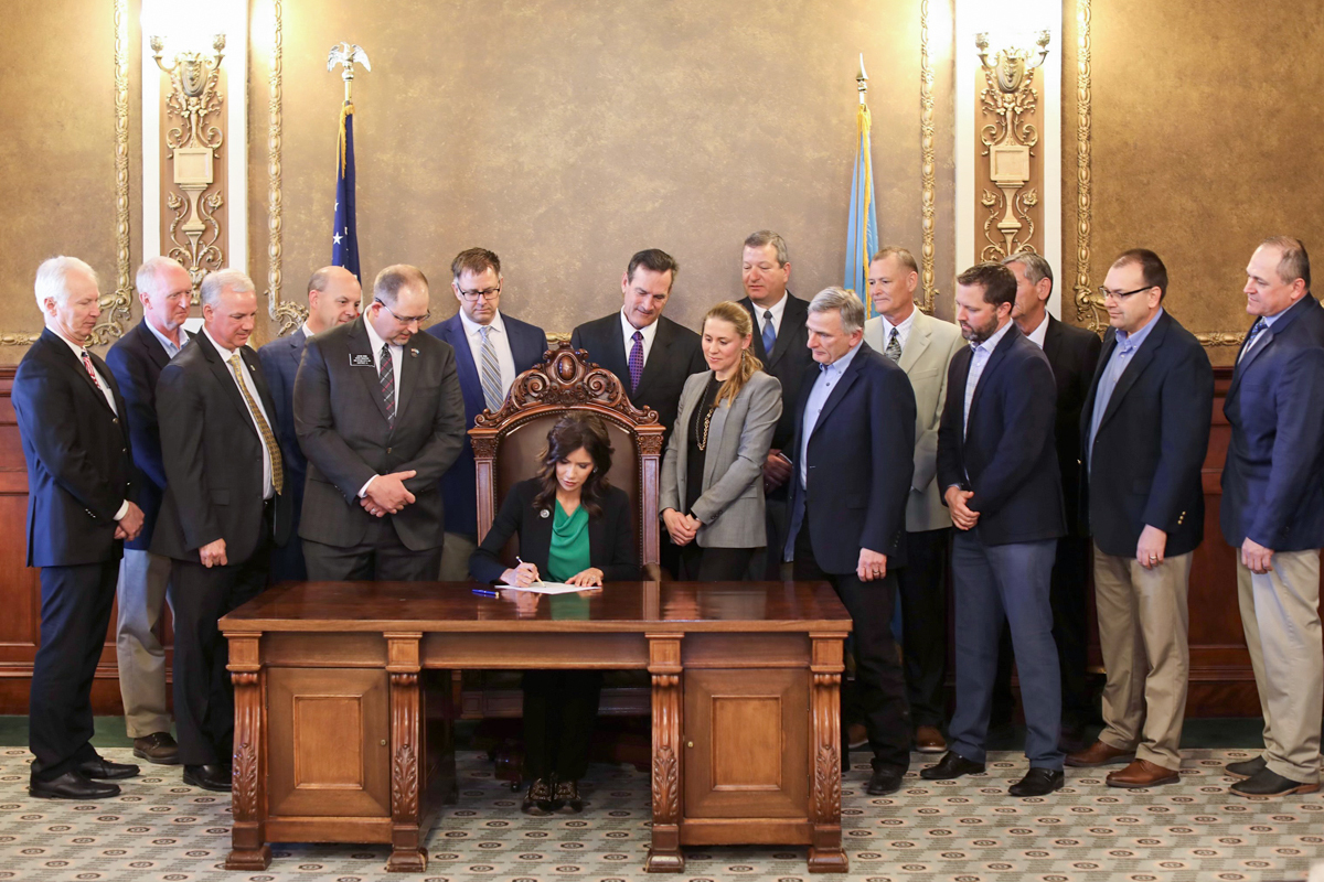 Governor Kristi Noem signs Senate Bill 34 at a desk surrounded by leaders in the telecommunications industry