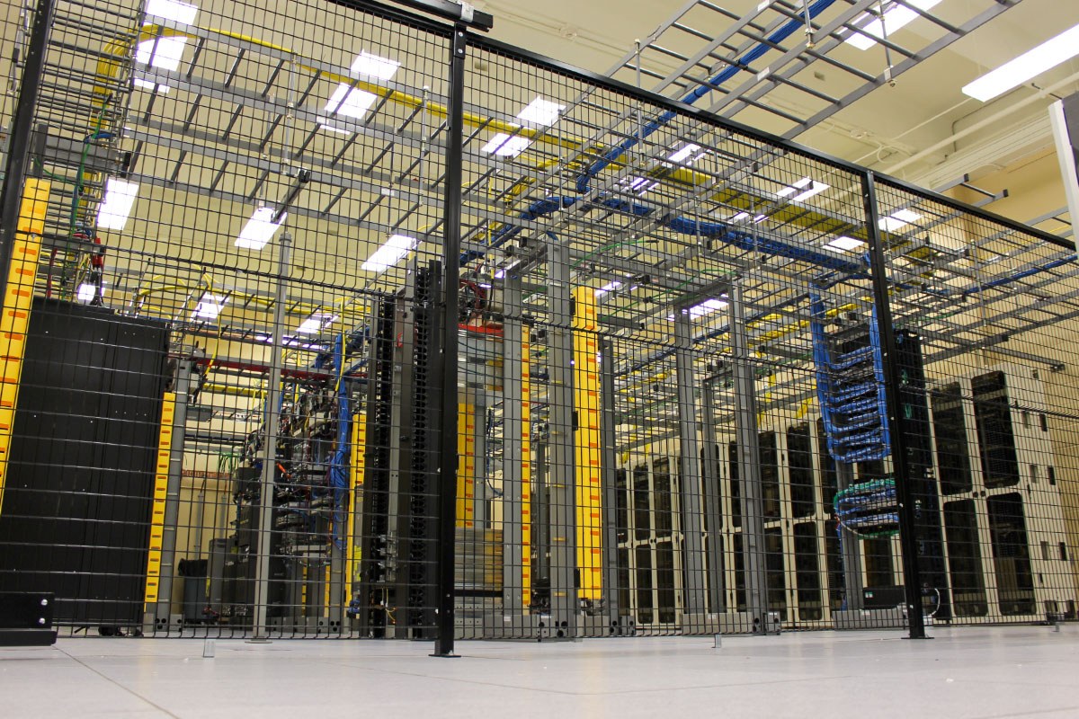 metal cage inside data center with racks and equipment behind it on a raised floor
