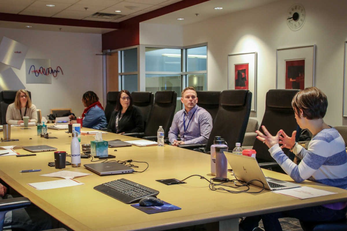 employees sitting around board room table listening to program facilitator