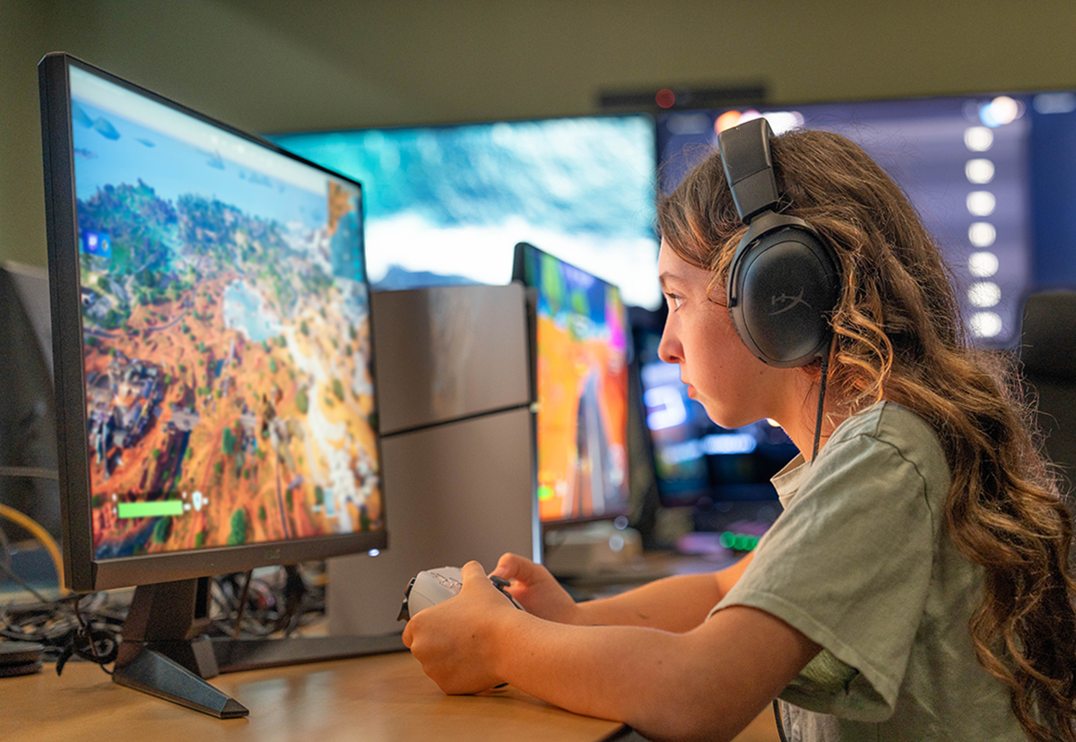 A girl holds a controller and looks at a monitor while playing the game Fortnite