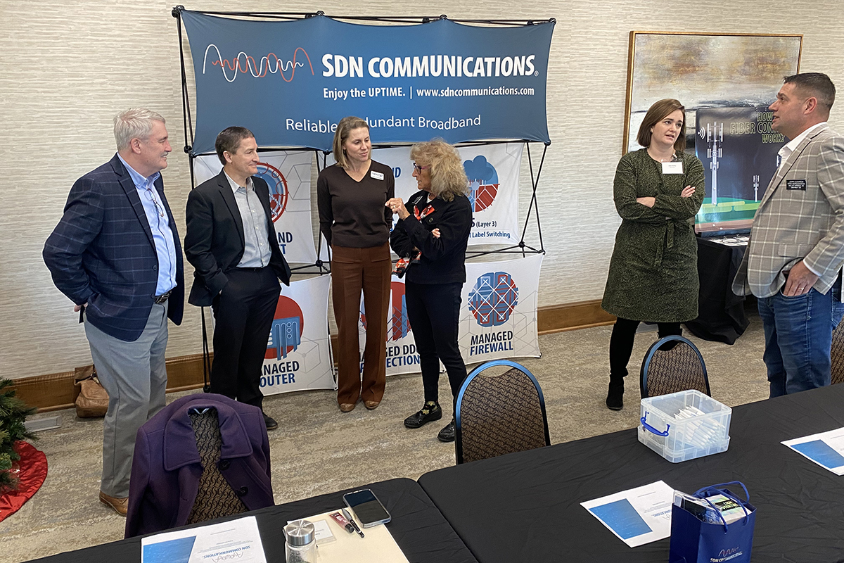 A group of people from the telecommunications industry mingle in a hotel ballroom in front of a SDN Communications sign.