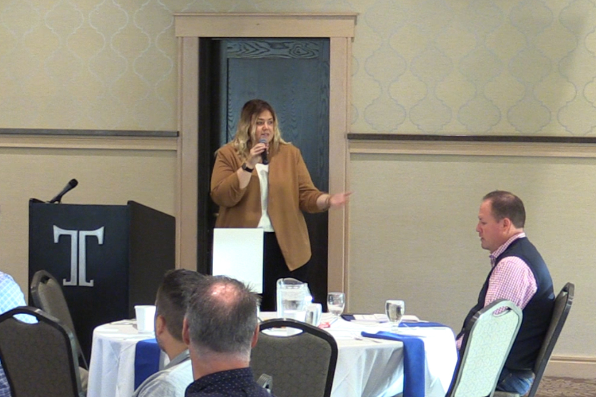 Jenean Michalov at the front of a banquet room speaking to employees