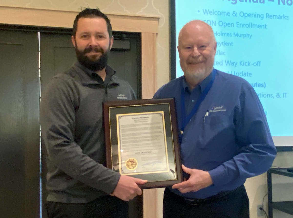 SDN Communications Director of Wholesame and Carrier Management Dan Eich presents a governor's proclamation to Russ Lampy