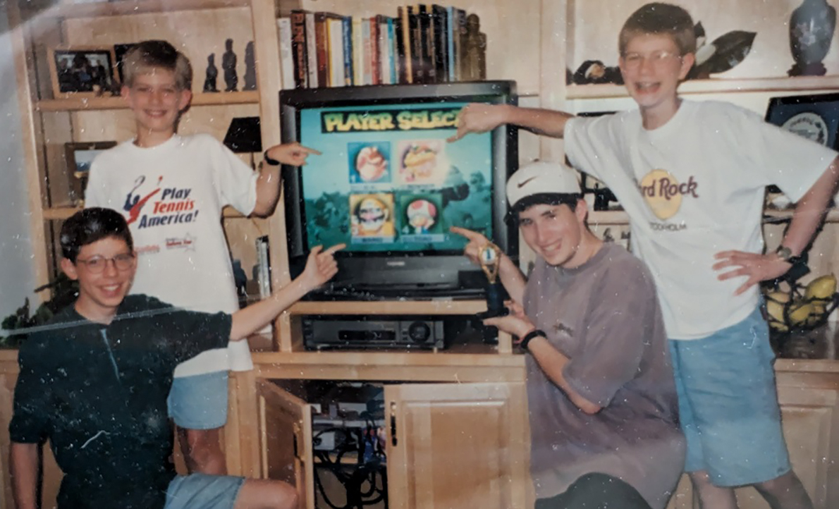 Four teenagers pose in front of a television showing Mario Kart 64 in a photo from the 1990s.