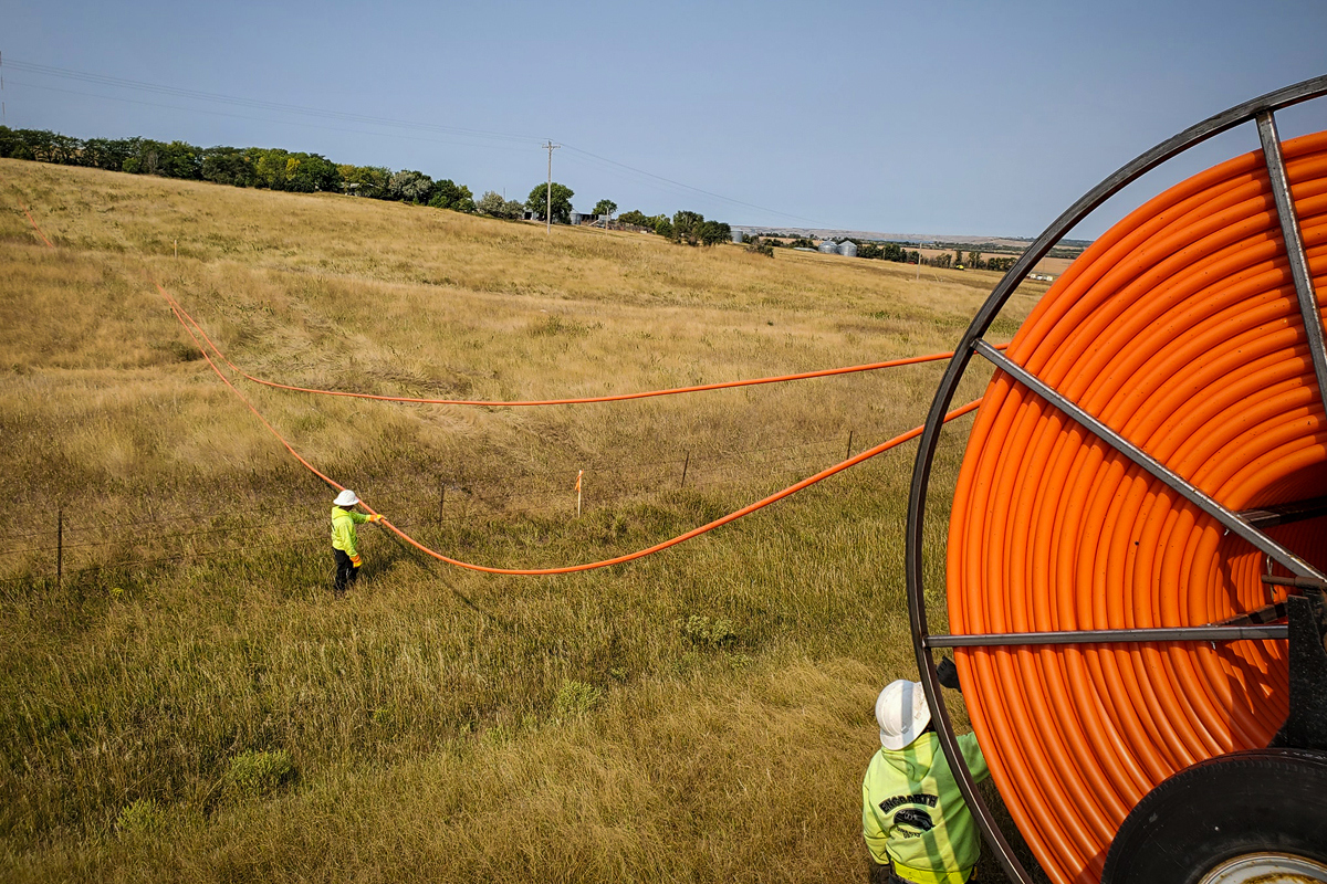 Bright orange fiber conduit being pulled through a field in rural Pierre