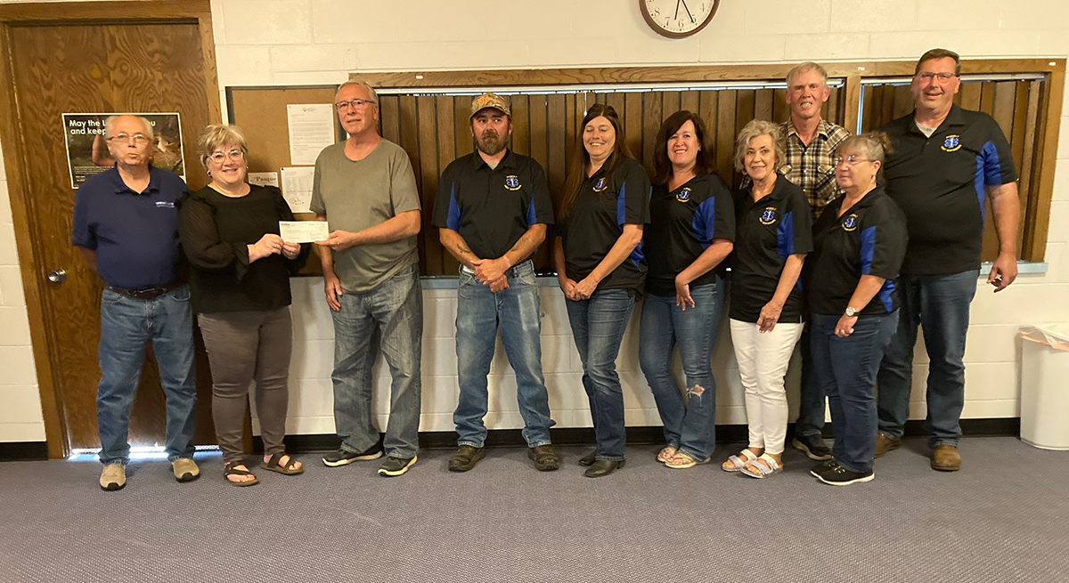 Venture Communications employees stand against a wall and hand a donation check to volunteer first responder crews in Rosholt.