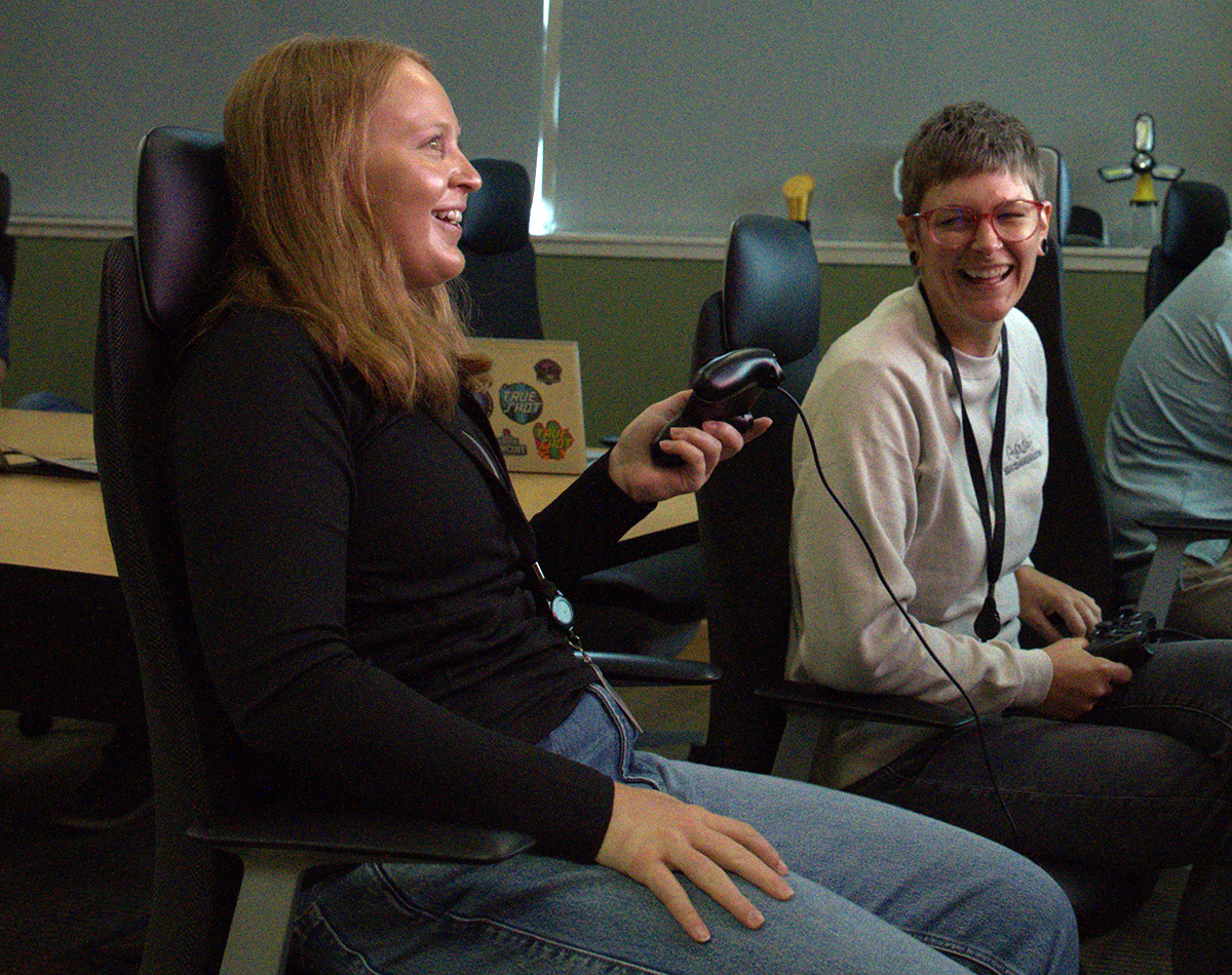 Two women sit on chairs and look at a TV screen.