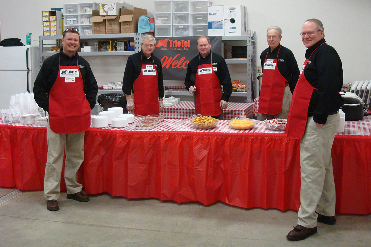 Five men with aprons stand behind a table and serve food