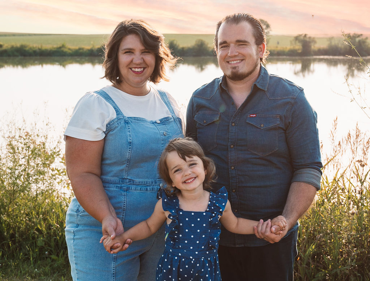 A family of three poses for a photo next to a body of water.