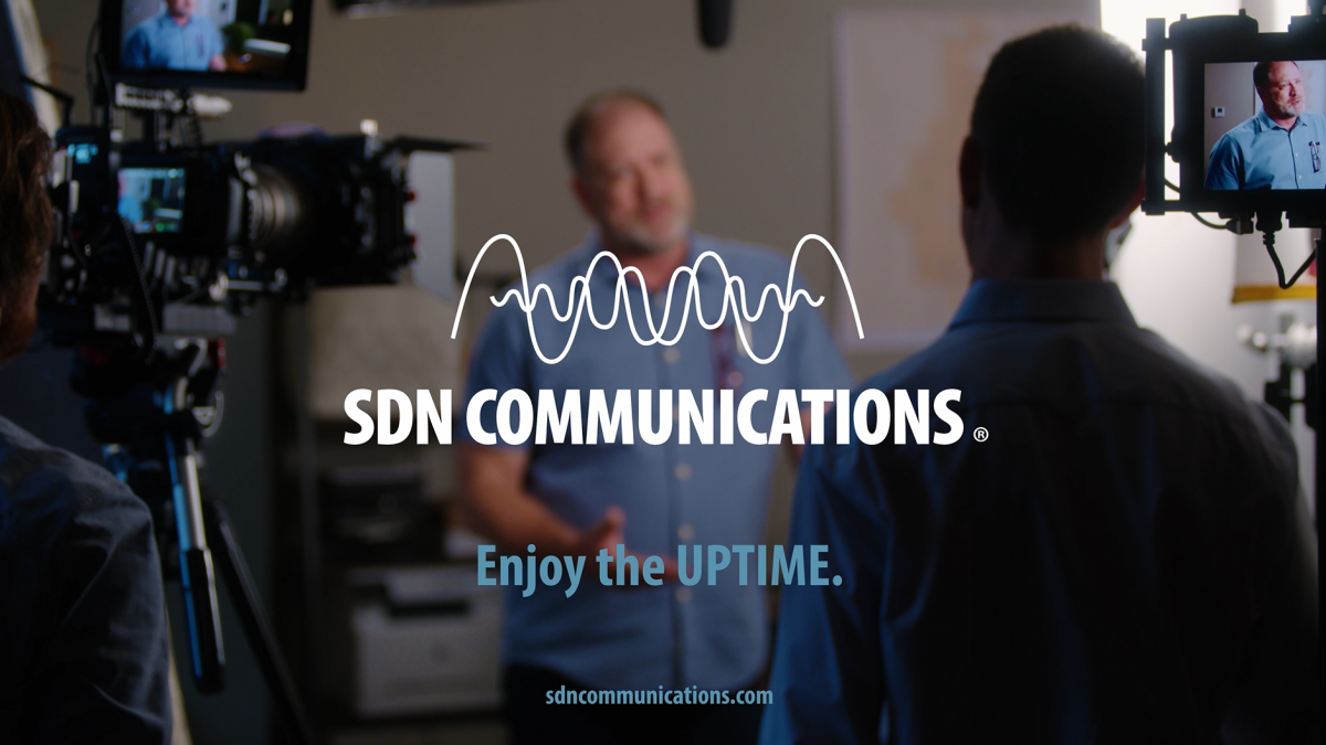 Screenshot from an SDN Communications commercial featuring a man being interviewed about SDN's services by a TV crew