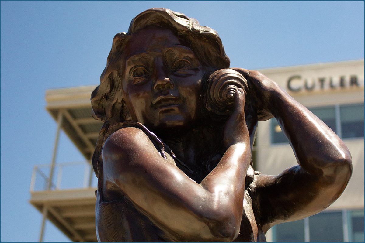 close view of sculpture's face as she holds a seashell up to her ear