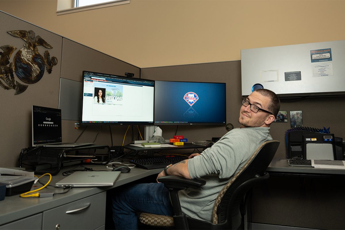 Eddie Cotton sits at desk working smiling at the camera