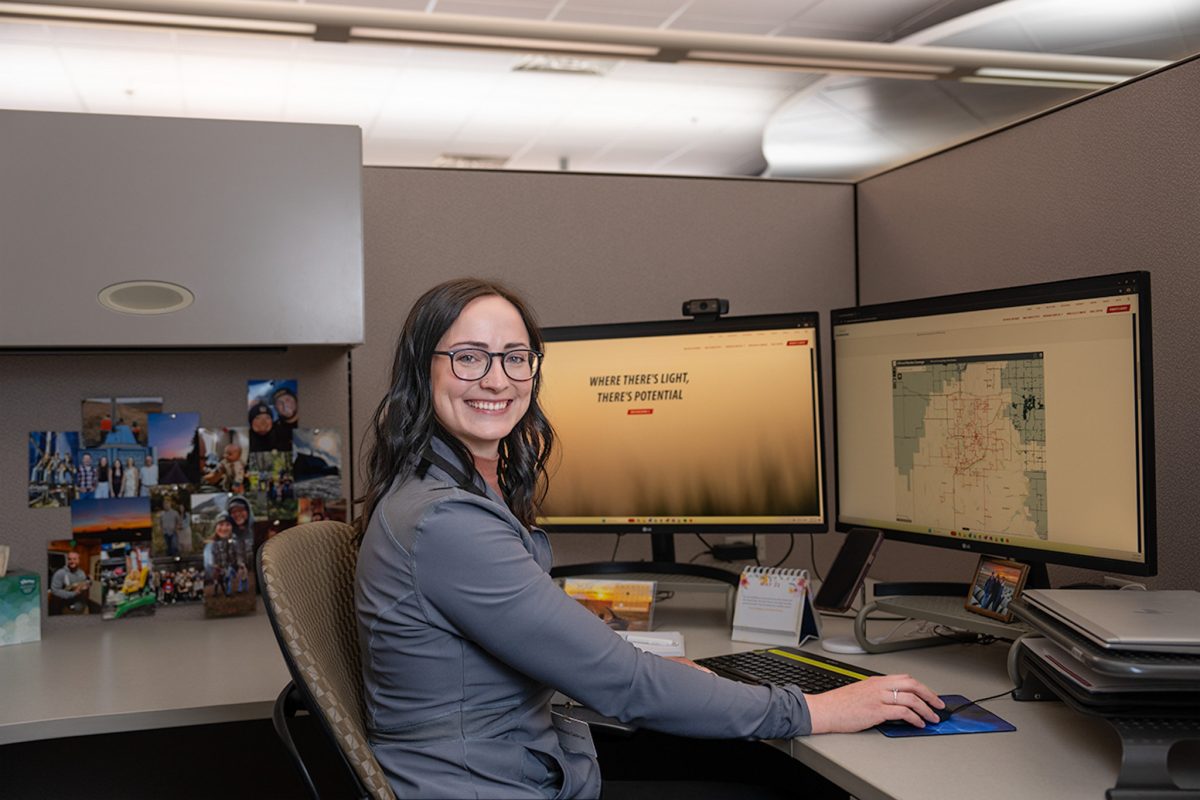 Melissa Dellman sits at desk working smiling at the camera