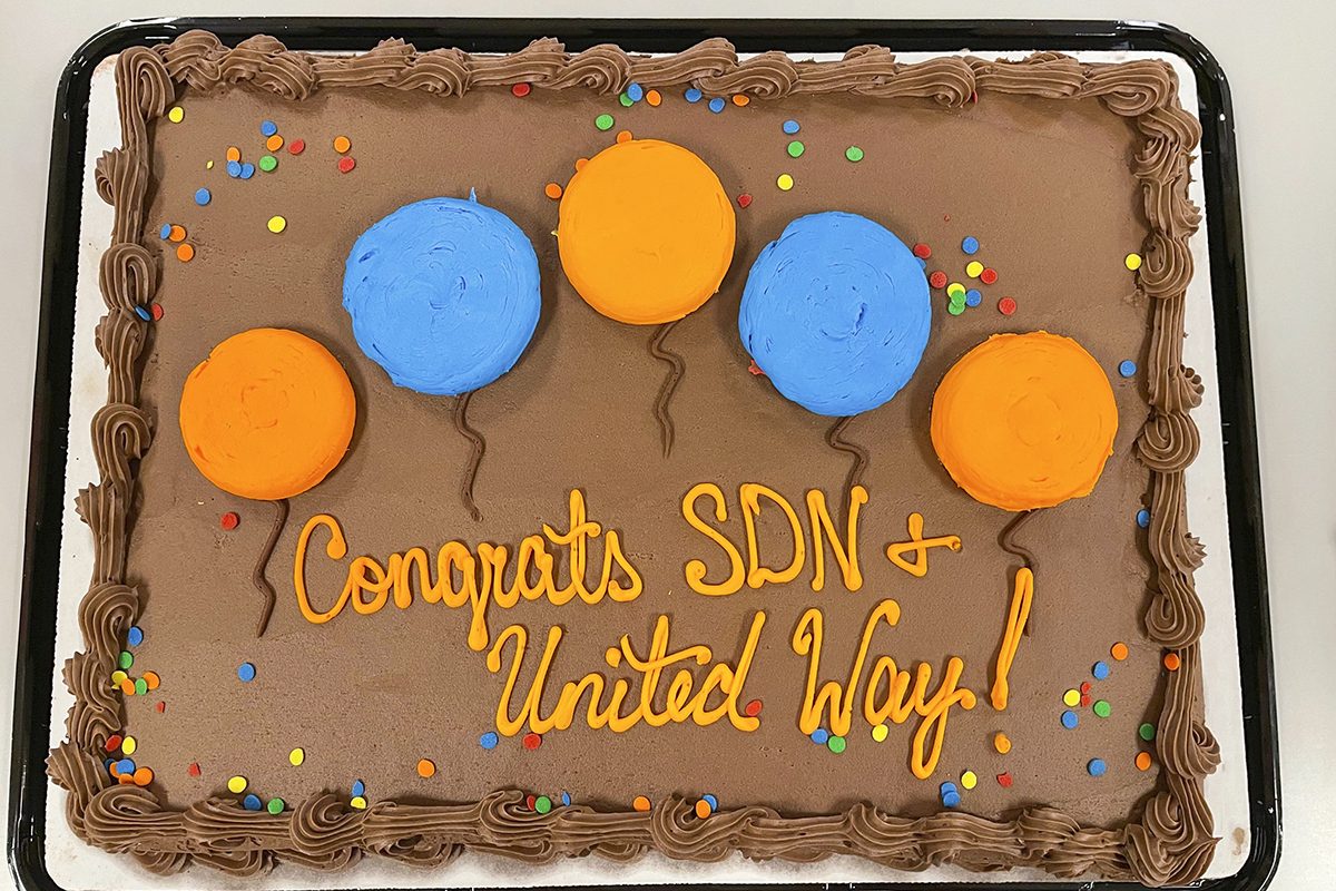 Chocolate-frosted sheet cake with Congratulations SDN and United Way written in icing with balloons