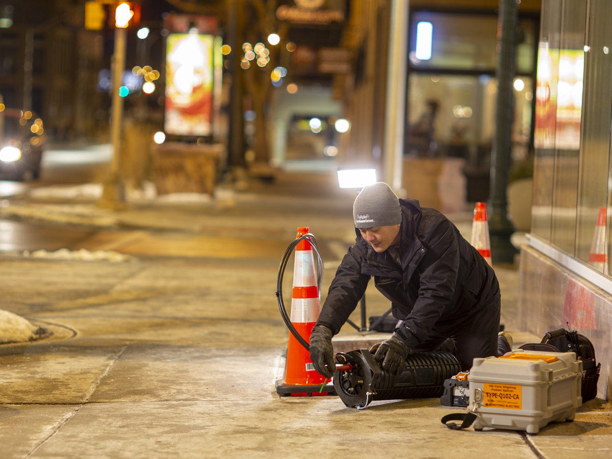 Employee working in a fiber box along a sidewalk