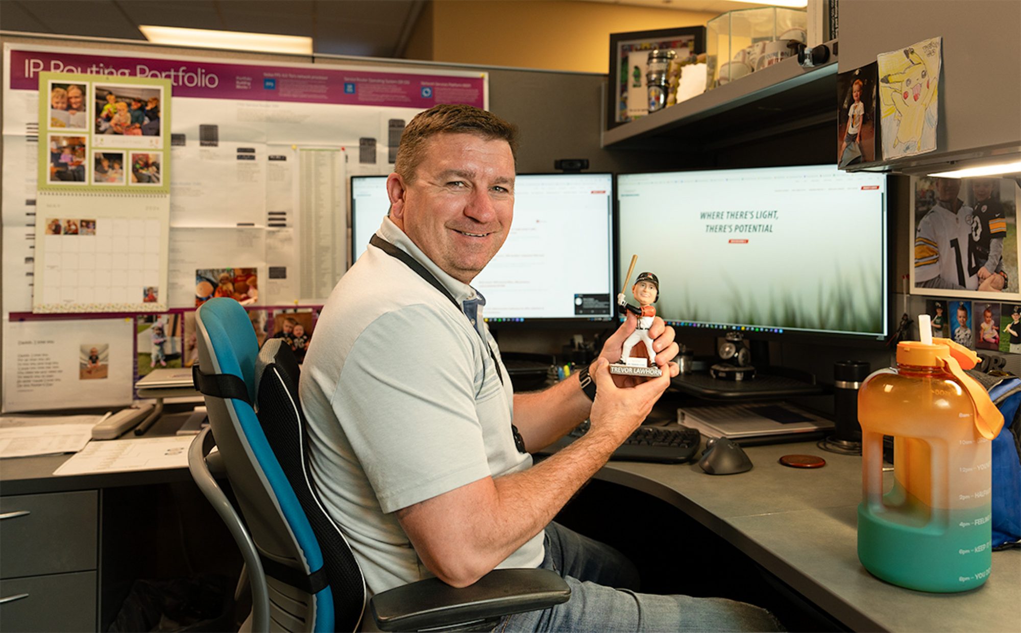 Trevor Lawhorn holds baseball player bobblehead while sitting at desk.