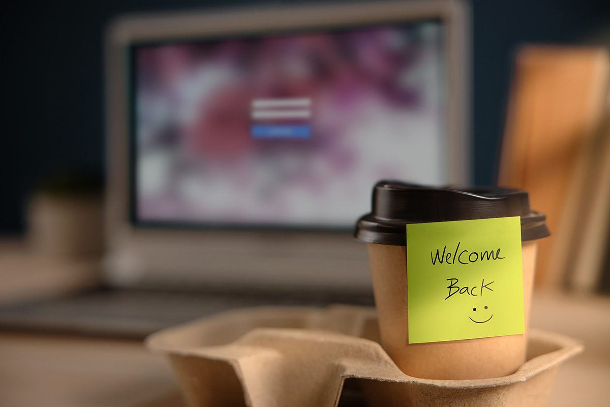 to-go coffee cup with welcome back post-it note in front of a computer screen